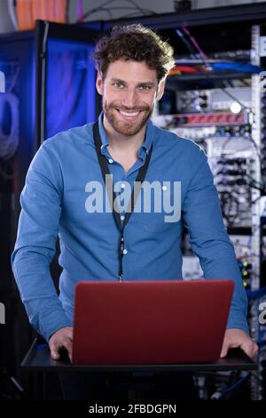Smiling male IT expertise standing in front of laptop at server room Stock Photo