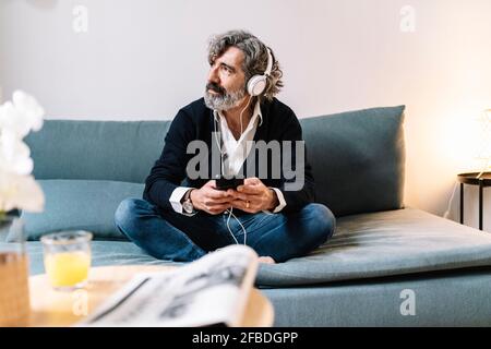 Thoughtful senior man looking away while using smart phone at home Stock Photo