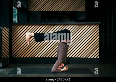 Male yoga instructor doing headstand in exercise room Stock Photo
