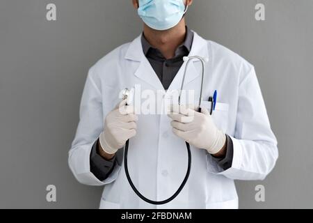 Male doctor wearing surgical glove holding stethoscope in front of wall Stock Photo