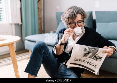 Senior man having coffee reading newspaper while sitting at home Stock Photo