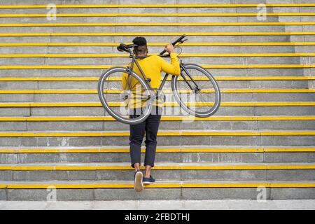 Young man carrying bicycle while climbing on staircase Stock Photo