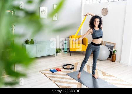 Young woman looking away while exercising with resistance band at home Stock Photo