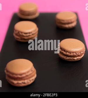 brown macarons with chocolate cream, on a black plate and a pink background Stock Photo