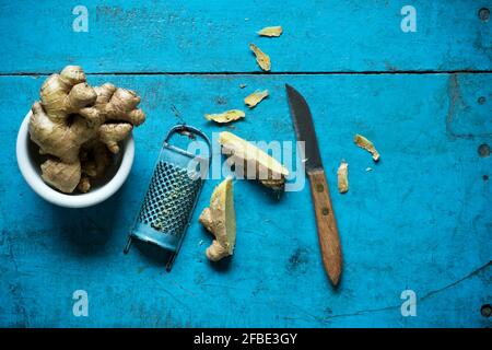 Ginger root, grater and kitchen knife lying on blue wooden surface Stock Photo