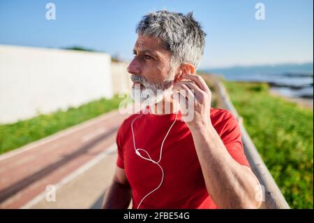Mature man with earphones looking away by the sea Stock Photo