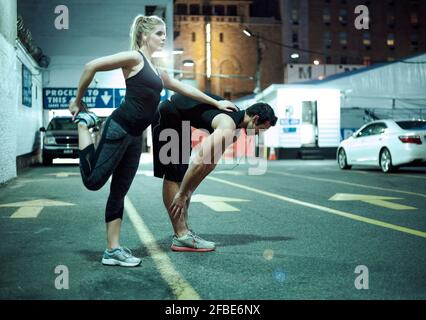 Couple doing stretching exercise during night on road in city Stock Photo