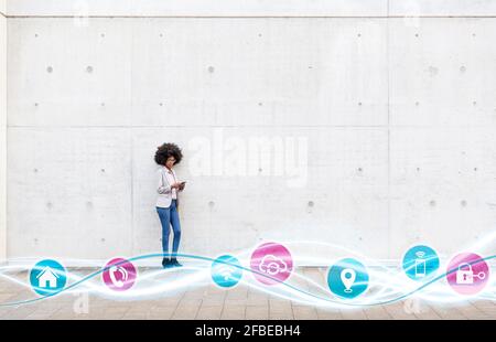 Female entrepreneur using mobile phone while standing with icons on glowing wave pattern by wall Stock Photo