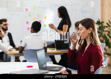 Young businesswoman drinking water while sitting by laptop in office Stock Photo