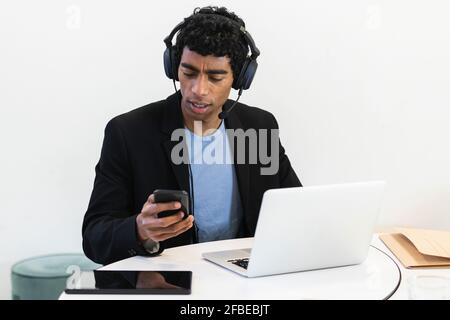 Young businessman with headset and laptop using mobile phone Stock Photo