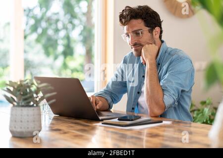 Serious male freelancer with head in hands working on laptop at home office Stock Photo