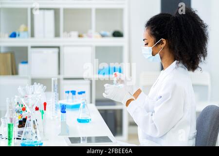 Young researcher doing scientific experiment in laboratory during pandemic Stock Photo