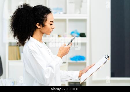 Young female researcher photographing paper on clipboard in laboratory Stock Photo