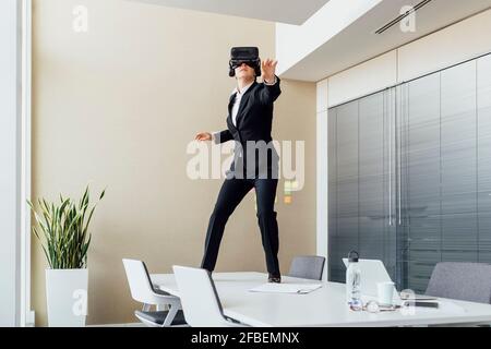 Female using virtual reality headset while standing on conference table in office Stock Photo