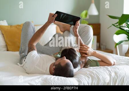 Relaxed young couple using digital tablet while lying on bed at home Stock Photo