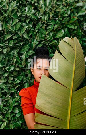 Woman looking through banana leaf while standing in front of green plants Stock Photo