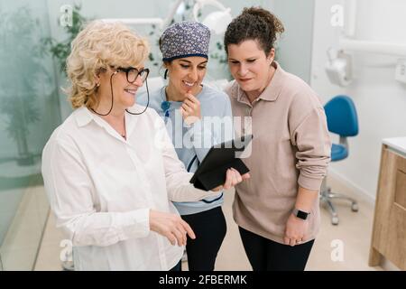 Smiling dentist using digital tablet while standing at clinic Stock Photo