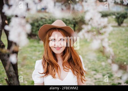 Smiling redhead woman wearing hat while standing at park Stock Photo