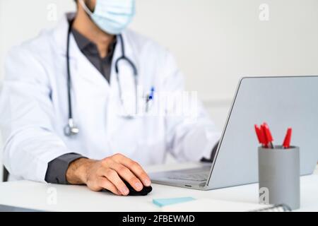Male healthcare worker in protective face mask using laptop Stock Photo