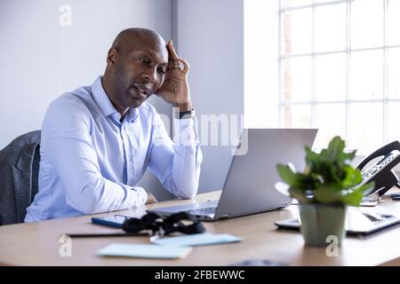 Tired businessman looking at laptop while sitting at desk in office Stock Photo