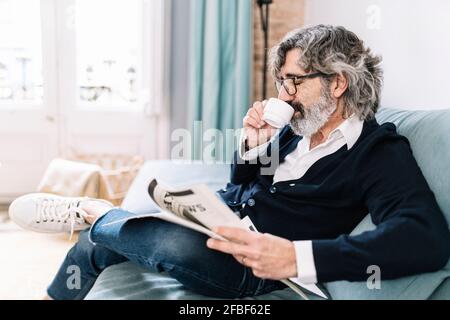 Man holding newspaper having coffee while sitting on sofa at home Stock Photo