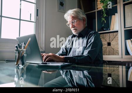 Serious senior male entrepreneur with eyeglasses using laptop in home office Stock Photo