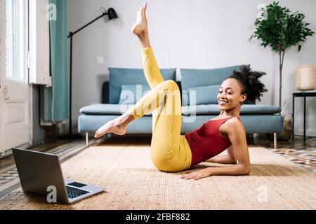 Smiling young woman exercising while watching tutorial on laptop at home Stock Photo