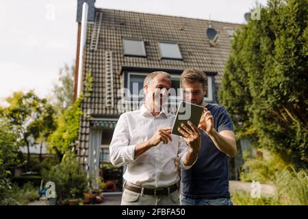 Happy father and son using digital tablet while standing in backyard Stock Photo