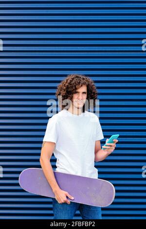 Caucasian young man using smart phone while holding skateboard Stock Photo