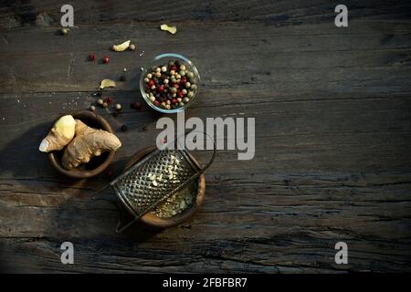 Bowls with ginger root, old grater and various peppercorns lying on wooden surface Stock Photo