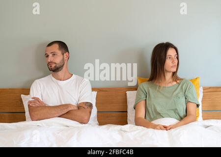 Frustrated young couple sitting on bed while looking away from each other at home Stock Photo