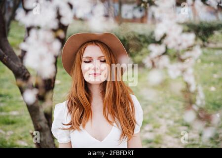 Redhead woman with eyes closed wearing hat at park Stock Photo