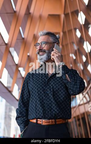 Smiling mature man with hand in pocket talking on mobile phone while looking away Stock Photo