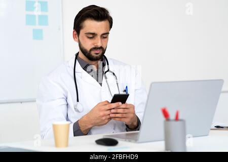 Male doctor using mobile phone while sitting at desk Stock Photo