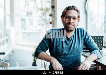 Confident man sitting by laptop in coffee shop Stock Photo