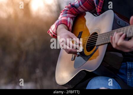 Male hands playing acoustic guitar on the natural park at the sunset. Selective focus. Stock Photo