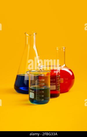 Flat bottom flask, conical flask and two Berzelius beaker glasses lay against mustard yellow background Stock Photo