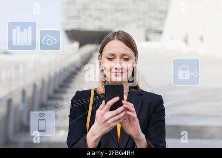 Businesswoman using mobile phone while standing with networking icon outdoors Stock Photo