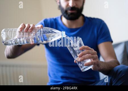 Thirsty young man pouring water in drinking glass at home Stock Photo