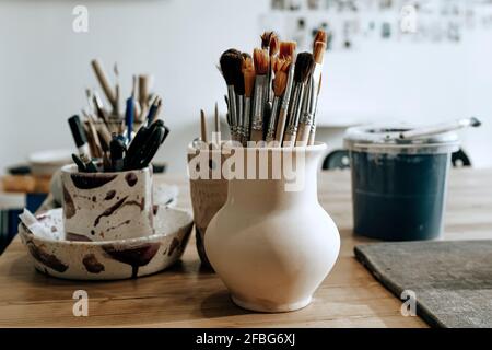 Ceramic utensils with brushes and other artisan tools on the table in art studio. Traditional pottery craft. Ceramics workshop concept Stock Photo