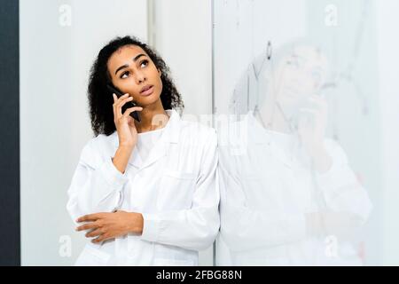 Young female doctor talking through smart phone while leaning on whiteboard in laboratory Stock Photo