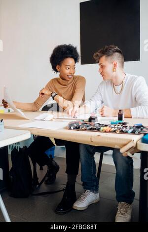 Smiling young woman talking with boyfriend while sitting at table in studio Stock Photo
