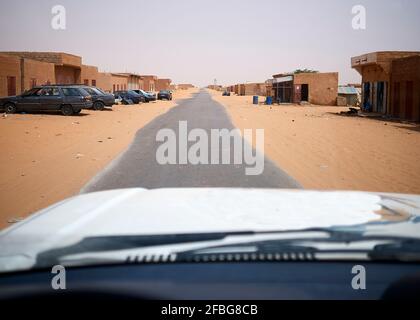 Car driving along asphalt road cutting through remote sandy town Stock Photo