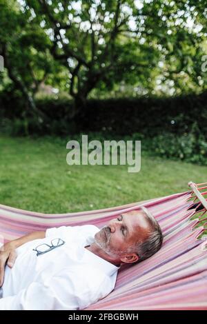 Mature man sleeping on hammock in backyard Stock Photo