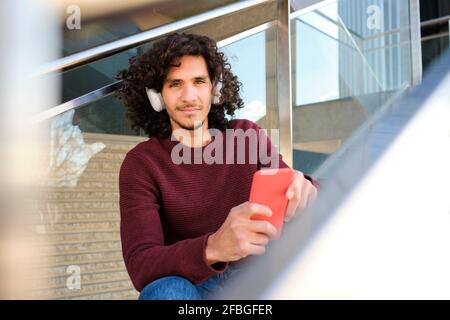Caucasian young man with headphones holding mobile phone at structure Stock Photo