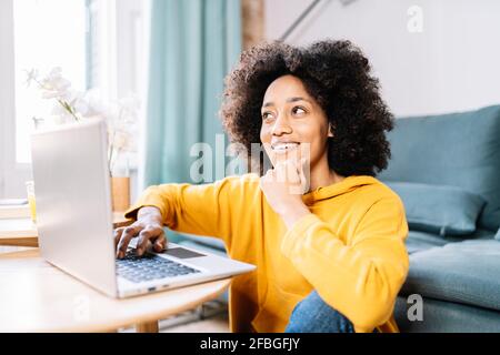 Thoughtful woman looking away while sitting by laptop at home Stock Photo