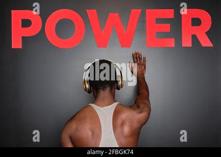 Man listening music through headphones while hand below power text on wall at gym Stock Photo