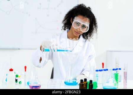 Female researcher pouring liquid in flask while experimenting at laboratory Stock Photo