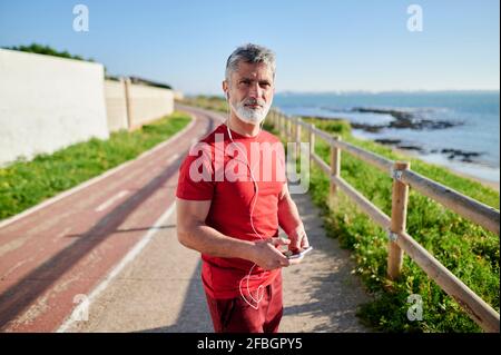 Mature man with smart phone standing on footpath near railing Stock Photo