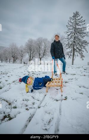 Smiling father looking at boy lying by sled on snow Stock Photo